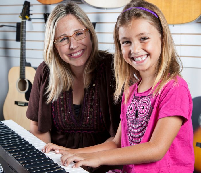 Woman teaching piano with a happy girl